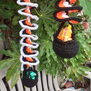 May include: Crocheted Halloween decorations. A black crocheted basket filled with candy hangs from a spiral-shaped decoration with white, orange, and black accents. Another similar decoration is visible in the image, with a basket filled with green wrapped candies.