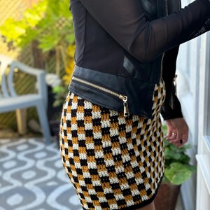 May include: A black leather jacket with a zip fastening and a checkered mini skirt in black, white and mustard yellow.