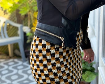 Peut inclure: Une veste en cuir noire avec une fermeture éclair et une mini-jupe à carreaux noirs, blancs et jaunes moutarde.