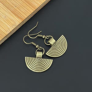 May include: A pair of gold-toned earrings with a half-circle design. The earrings have a textured, grooved surface and hang from a simple hook.