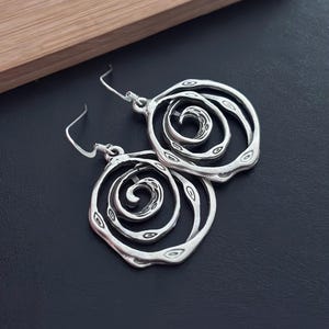 May include: Silver earrings with a spiral design. The earrings are made of a textured metal and have a circular shape.