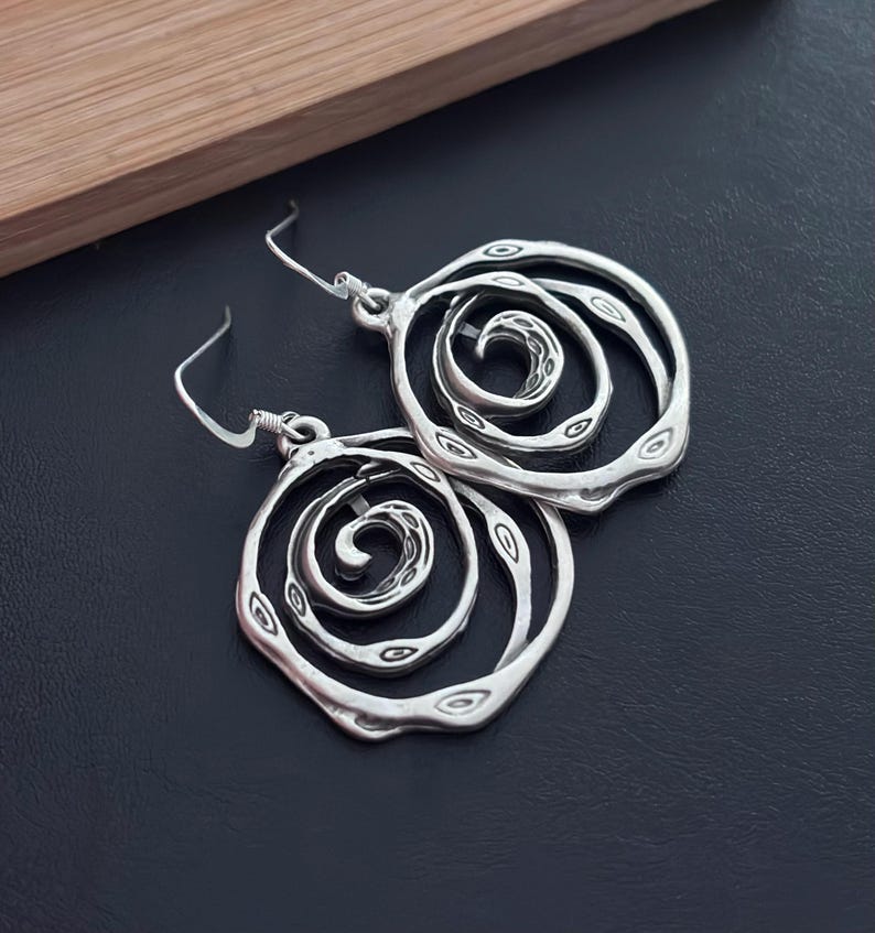 May include: Silver earrings with a spiral design. The earrings are made of a textured metal and have a circular shape.