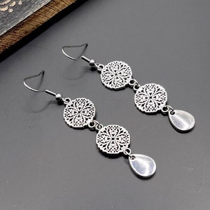 May include: Silver dangle earrings with three round, filigree charms and a teardrop-shaped charm at the bottom of each earring.