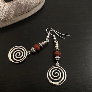 May include: Silver earrings with a spiral design and red beads.