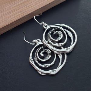 May include: Silver earrings with a spiral design. The earrings are made of metal and have a textured finish.