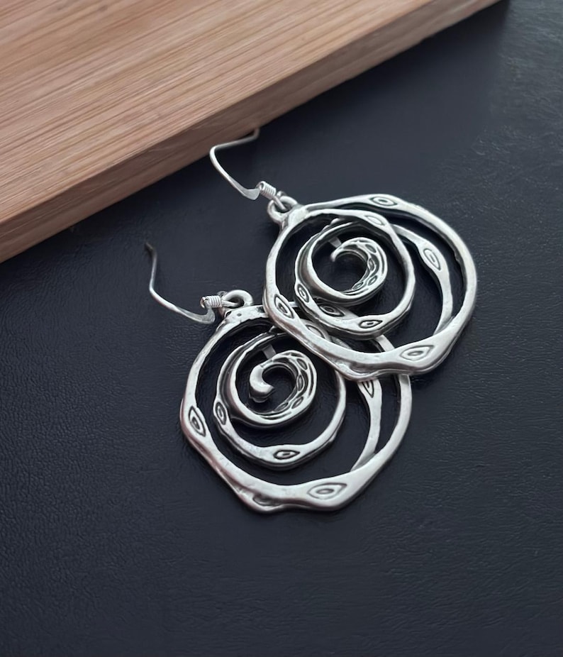 May include: Silver earrings with a spiral design. The earrings are made of metal and have a textured finish.