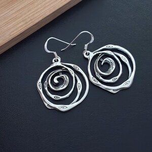 May include: Silver earrings with a spiral design. The earrings are round and have a textured surface.