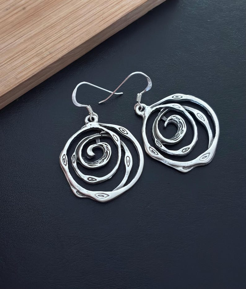May include: Silver earrings with a spiral design. The earrings are round and have a textured surface.