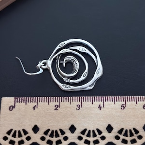 May include: Silver tone spiral design earrings with a hook closure. The earrings are approximately 2 inches in diameter.