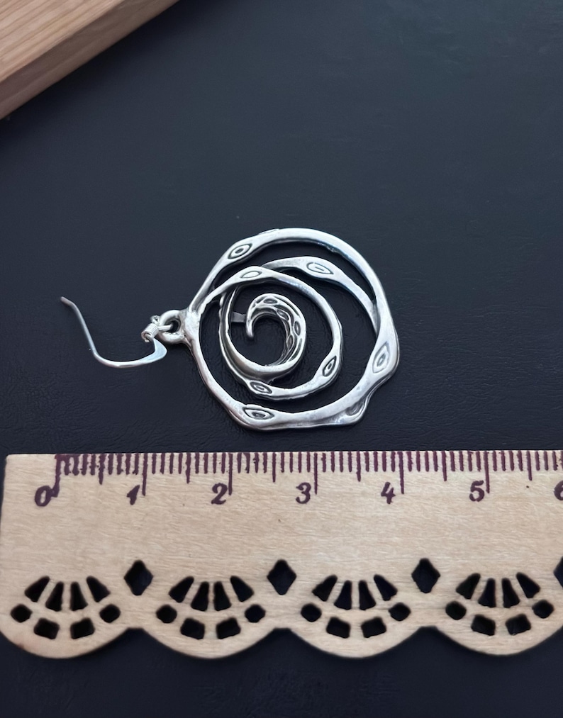 May include: Silver tone spiral design earrings with a hook closure. The earrings are approximately 2 inches in diameter.