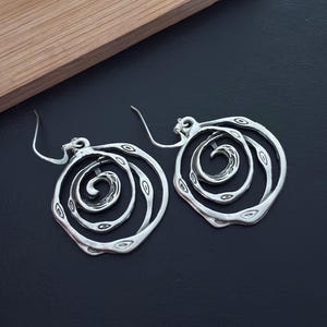 May include: Silver earrings with a spiral design. The earrings are made of metal and have a circular shape.