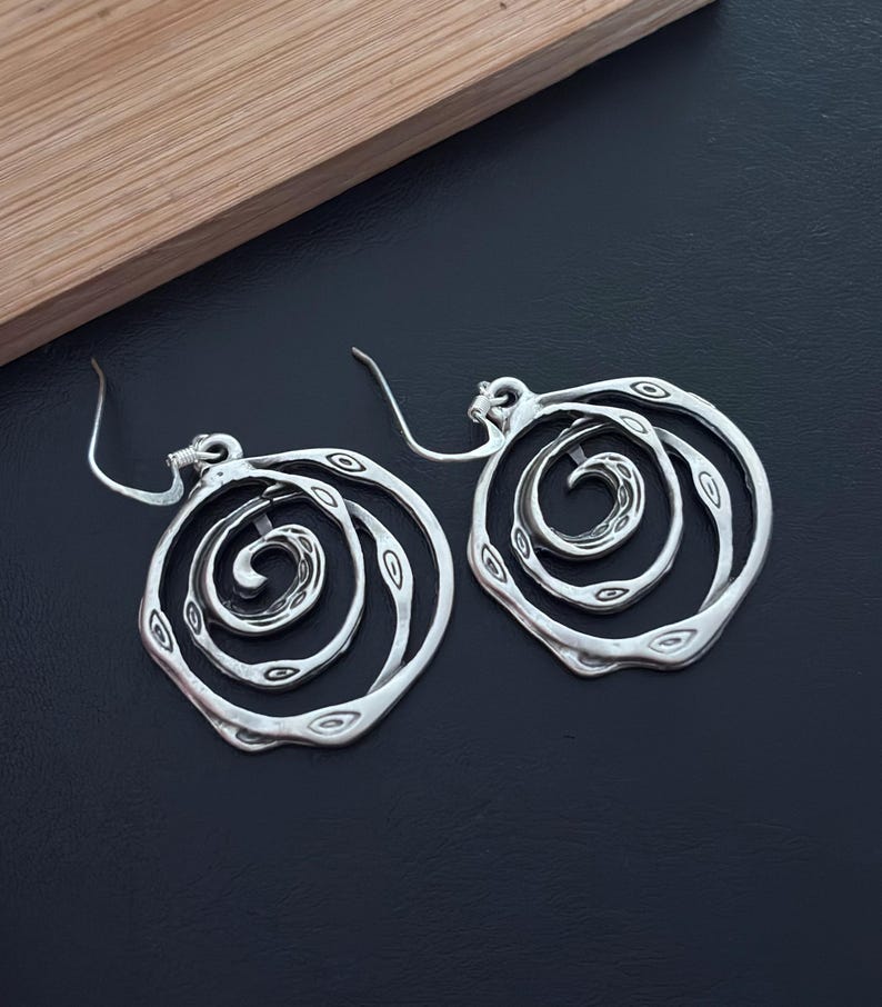 May include: Silver earrings with a spiral design. The earrings are made of metal and have a circular shape.