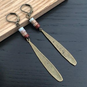 May include: A pair of long, bronze earrings with a teardrop shape. Each earring has a cluster of four small, round, multi-colored beads.