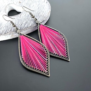 May include: A pair of pink and white thread earrings with a bronze metal frame in the shape of a teardrop.