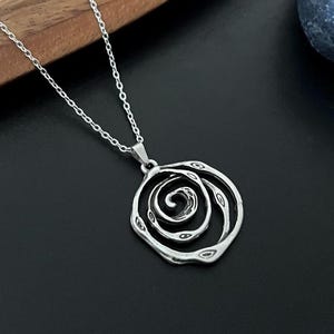 May include: A silver necklace with a pendant featuring a spiral design. The pendant is made of multiple overlapping circles, creating a textured and intricate look.