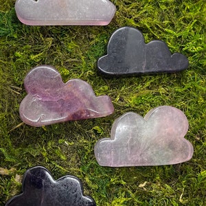 May include: Five cloud-shaped crystal stones in various shades of purple, pink, and black. The stones are arranged on a bed of green moss.