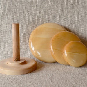Op de afbeelding: Drie houten garenkommen in verschillende maten, met een houten garenmolen op de achtergrond. De kommen zijn lichtbruin en hebben een gladde, gepolijste afwerking.