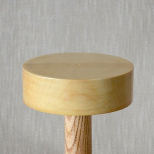 Op de afbeelding: Een houten hoedenstandaard met een ronde, lichtbruine bovenkant en een cilindrische basis.