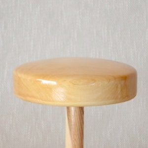 Op de afbeelding: Een houten spinnewiel met een ronde, lichtbruine bovenkant en een cilindrische, lichtbruine basis.