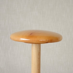 Op de afbeelding: Een houten hoedenstandaard met een ronde, lichtbruine bovenkant en een cilindrische basis.