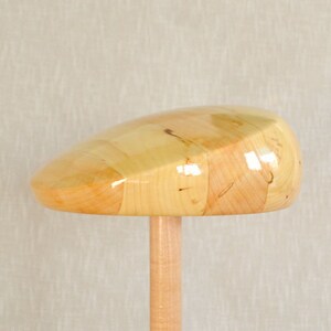 Op de afbeelding: Een houten hoedblok met een lichtbruine afwerking. Het blok is gevormd als een traditionele pet en heeft een glad, gepolijst oppervlak.