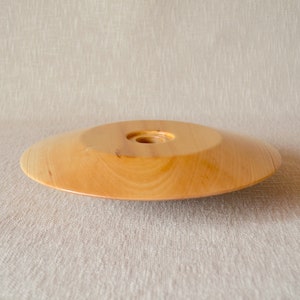 May include: A light brown wooden plate with a small hole in the center. The plate is slightly curved and has a smooth surface.