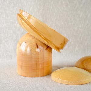 May include: A set of wooden decorative objects. The set includes a cylindrical base with a curved top piece and two smaller, rounded pieces. The wood has a light, natural color and visible grain.