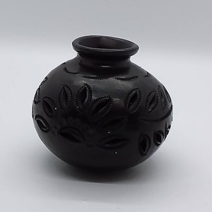 Peut inclure: Vase en céramique noire avec des découpes florales complexes. Le vase est rond et a une petite ouverture en haut.