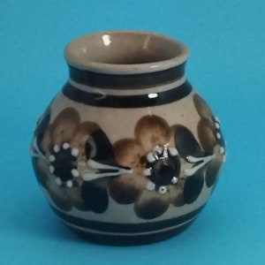 May include: A small, brown and white ceramic vase with a floral design. The vase has a rounded body and a narrow opening.