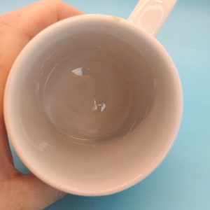 May include: White ceramic mug with a handle. The mug is empty and clean.