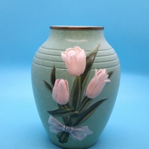 May include: A green ceramic vase with a gold rim and a painted design of pink tulips and a green bow.
