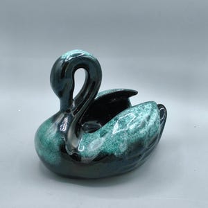 May include: A ceramic swan figurine featuring a glossy finish with a deep black base colour and mottled teal and turquoise highlights. The swan is depicted with its neck curved gracefully, and the body includes a hollow centre section.