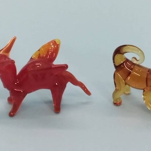May include: Two glass animal figurines. A red dragon with orange wings and a brown monkey with a curled tail.