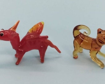 May include: Two glass animal figurines. A red dragon with orange wings and a brown monkey with a curled tail.