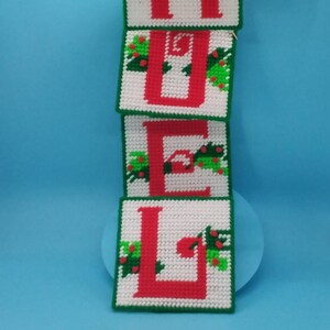May include: Four red felt squares with white letters spelling "H O M E" with green holly and berries around each letter.