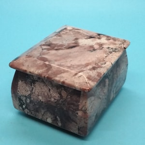 May include: A small, square, pink and brown marble trinket box with a hinged lid.