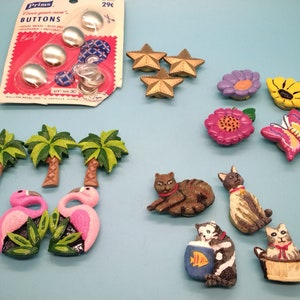 May include: A selection of decorative buttons and embellishments in various shapes and colours. Includes silver buttons, star-shaped buttons, flower and butterfly designs, palm trees, flamingos, and cat figurines. The packaging reads "Prims Buttons".