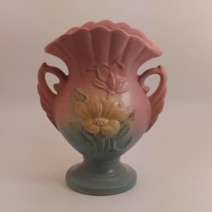May include: A pink and blue ceramic vase with two handles and a floral design. The vase has a scalloped rim and a base with a floral design.