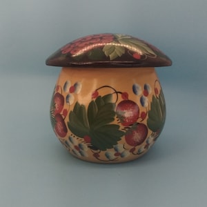 May include: A hand-painted wooden jar with a lid, decorated with a floral pattern of red berries and green leaves on a yellow background. The lid is painted with a cluster of red berries.