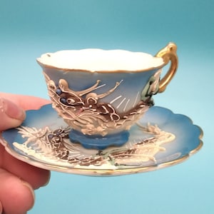 Peut inclure: Une tasse à thé et une soucoupe en bleu et blanc avec un bord doré. La tasse et la soucoupe sont décorées d'un motif en relief de dragon.