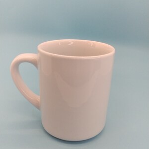 May include: A white ceramic mug with a rounded handle. The mug is empty and sitting on a light blue surface.