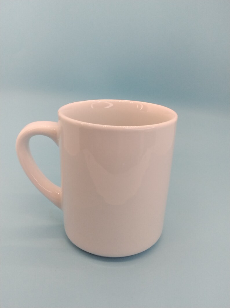 May include: A white ceramic mug with a rounded handle. The mug is empty and sitting on a light blue surface.
