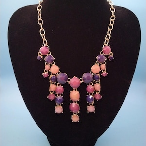 May include: A gold chain necklace with a cascading design of pink, purple, and blue faceted stones.