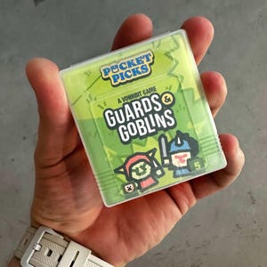 May include: A green and white card game called "Guards & Goblins", a Vonnbit game, from the Pocket Picks series. The card features a cartoon illustration of a goblin and a guard.