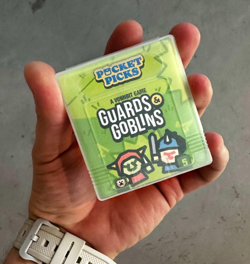 May include: A green and white card game called "Guards & Goblins", a Vonnbit game, from the Pocket Picks series. The card features a cartoon illustration of a goblin and a guard.