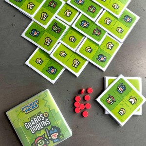May include: A green and yellow board game called "Pocket Picks: Guards & Goblins". The game includes a variety of cards with illustrations of guards and goblins. There are also red game pieces.