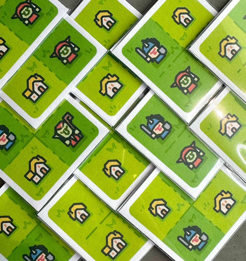 May include: A collection of white cards with green backgrounds featuring pixelated illustrations of houses, warriors, and other characters. The cards are stacked in a diagonal pattern.