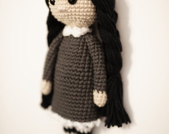 May include: A crocheted doll with black hair, a grey dress, white and black striped leggings, and black shoes.