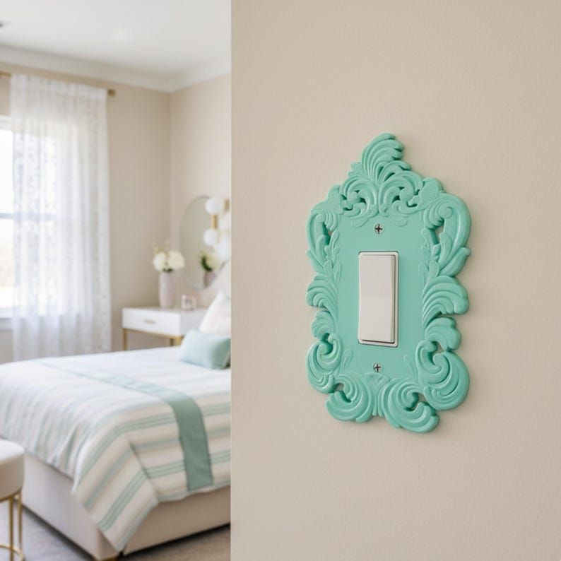 May include: A decorative light switch cover in a bedroom setting. The cover is a vibrant turquoise color with ornate, swirling details. It surrounds a white light switch, adding a touch of elegance to the wall.