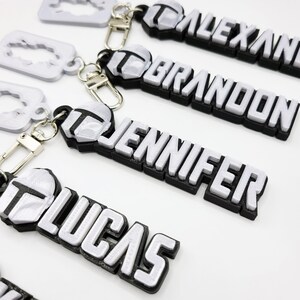 May include: Four silver keychains with black trim, each featuring a different name:  "ALEXANDRIA", "BRANDON", "JENNIFER", and "LUCAS".